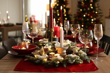 Christmas table setting with stylish dishware, glasses and burning candles in festive decorated room