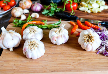 five heads of garlic on a cutting board with various vegetables
