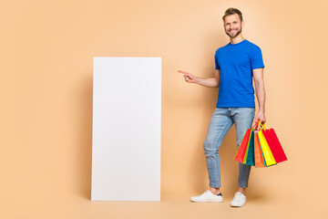 Full length portrait of handsome man direct finger empty space display hold packages isolated on beige color background