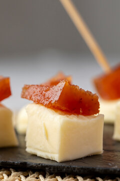 A delicious snack of creamy cheese topped with a slice of quince paste, elegantly presented on a dark slate board, perfect for gourmet finger food presentations.