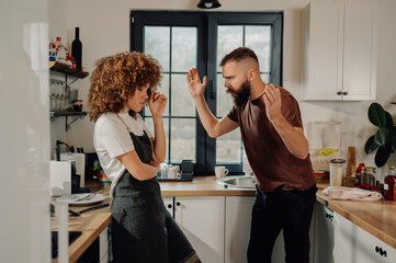 Young couple arguing in kitchen, frustrated woman listening to man screaming