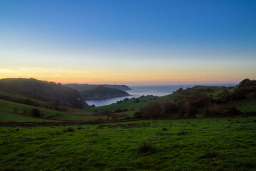 Atardecer en bah&iacute;a tras prados verde en litoral de Asturias