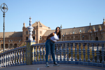 young, beautiful, brunette moroccan woman dressed in white top and jeans in Seville's Spain square. Woman enjoys her vacation walking around the city in andalusia, Spain. Travel and tourism concept.