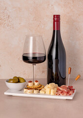 Food photography of red wine with cheese parmesan, prosciutto, olives; crackers with soft cheese; wine glass with bottle, assortment of appetizers for a party, celebration