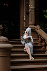 Elegant Woman Dressed in Comfortable Robe is Reading Newspaper Sitting on Steps