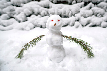 Obraz premium Small snowman made with fresh snow and pine branch arms on frosty day in winter setting. Handmade snowman with red eyes made of barberries fruits and nose made of pine cone. Snow-covered outdoor scene
