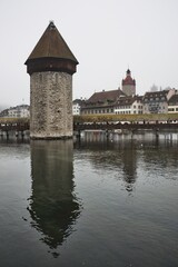 The iconic Water Tower and Chapel Bridge in the historic center of Lucerne, Switzerland, reflected in the calm waters on a foggy day. A timeless blend of medieval architecture and serene atmosphere.
