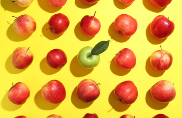 Flat lay composition with green apple surrounded by red ones on yellow background