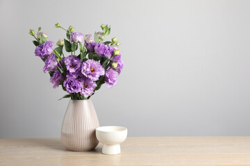 Vase with beautiful eustoma flowers on wooden table, space for text