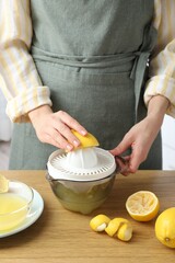 Woman with lemon using juicer at wooden table, closeup