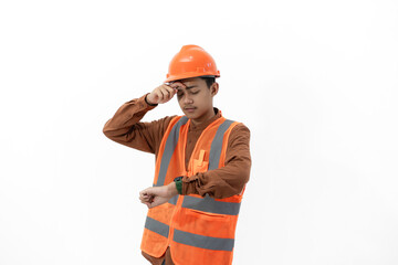 Young Indonesian male construction worker in full safety gear looking tired looking at time on his watch, industrial and construction concept, isolated on white background.