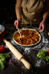 Person preparing homemade pizza with fresh ingredients in the kitchen