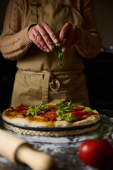 Chef garnishing homemade pizza with fresh basil leaves in warm kitchen