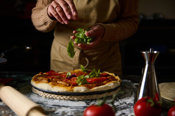 Chef adding fresh basil to homemade pizza in rustic kitchen setting