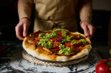 Person serving fresh homemade pizza topped with basil and tomatoes