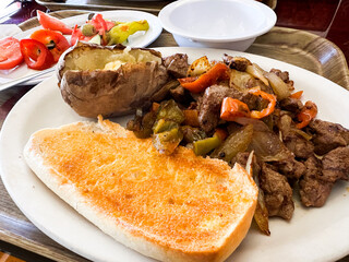 Delicious meal featuring grilled beef, vegetables, baked potato, and toast served at local eatery during lunchtime