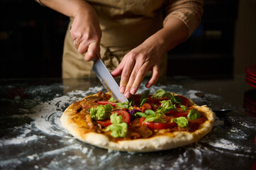 Chef slicing freshly baked pizza with toppings in kitchen