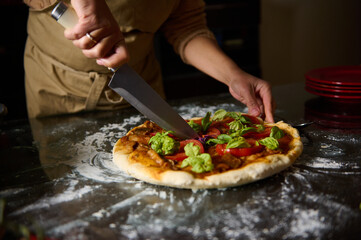 Person slicing freshly made pizza with a large knife on a floured surface