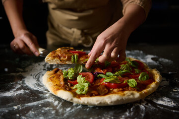 Chef slicing fresh homemade pizza with basil and tomatoes