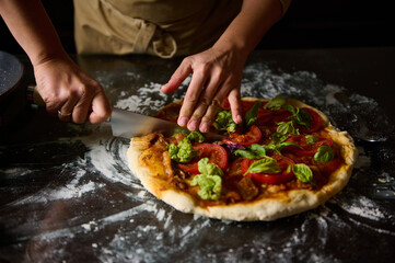 Chef slicing homemade pizza on rustic kitchen countertop