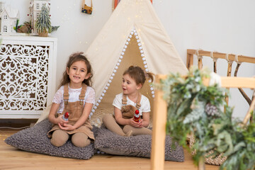 two little girls in a wigwam, wigwam together at home in children playroom. Friends talk hold textbook. © Маргарита Медведева