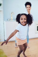 Cheerful black girl running and leading mother while looking ta camera