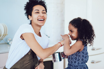 Joyful mother playing with daughter in kitchen while cooking