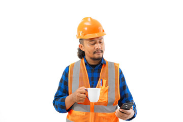 Indonesian male construction worker in full safety gear making voice call while enjoying a cup of coffee while working, construction and industrial work concept, isolated on white background.