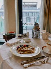 Delicious hotel breakfast with crepes, berries, cityscape backdrop