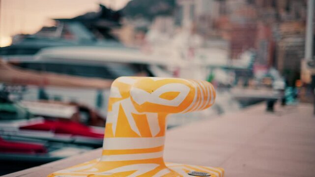 Close up of a white and yellow dock cleat in a harbour with boats on the background