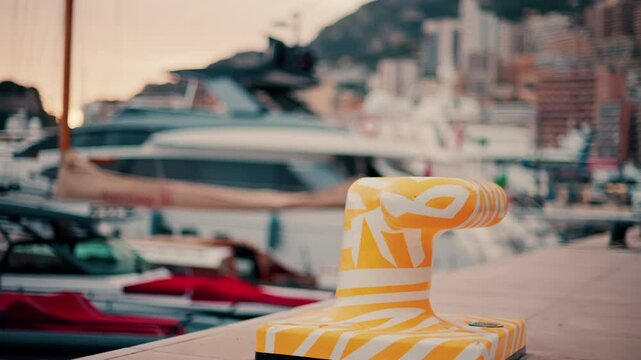 Close up of a white and yellow dock cleat in a harbour with boats on the background