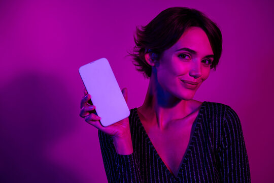 Photo portrait of pretty young girl hold white screen device wear trendy overall outfit isolated on neon light pink color background