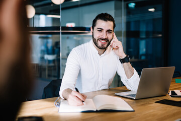 Obraz premium Cheerful successful manager writing notes at table in office
