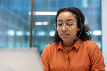 A professional woman wearing a headset, engaging in a call at her computer. The office setting...