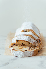 Traditional German Christmas cake Stollen sliced into pieces with raisins, fruits and nuts inside and sprinkled with powdered sugar on the white background