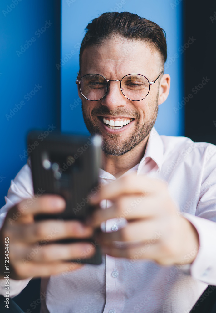 Aufkleber happy male influencer in eyewear reading funny messages during mobile chatting indoors, caucasian bl