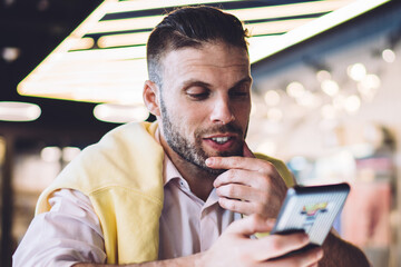 Caucasian male freelancer in smart casual wear using cellular device for online mobility and...
