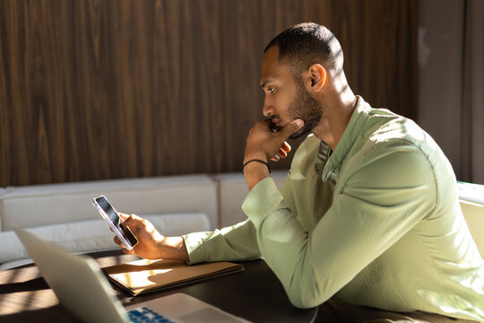 Confident man using laptop and mobile phone while working in office
