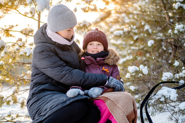 Mother and daughter are sitting on a sleigh in the winter forest on Christmas holidays. Active winter holidays with children on winter holidays.