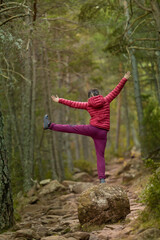 A woman is standing on a rock in a forest, with her arms raised in the air