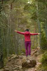 A woman in a red jacket is standing on a rock in a forest