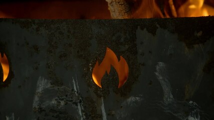 Through a hole in the shape of a fire in an old, rusty brazier, one can see how the flames are burning. Slow motion. Close-up - Powered by Adobe