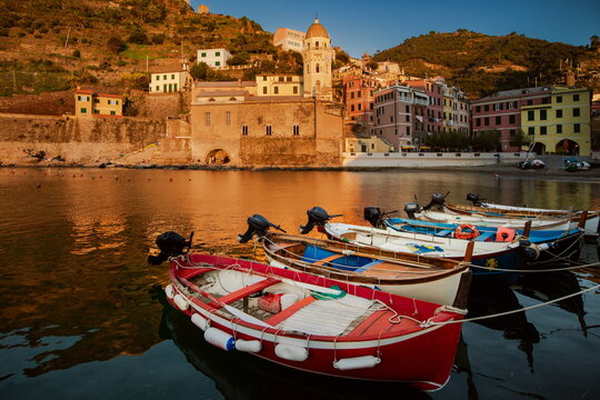 Fishing boats flood the Vernazza bay, with Chiesa di Santa Margherita di Antiochia in the background, in Cinque Terre, Italy, at sunset.