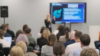Group of professionals listening to keynote speaker during business conference. Presentation screen visible.