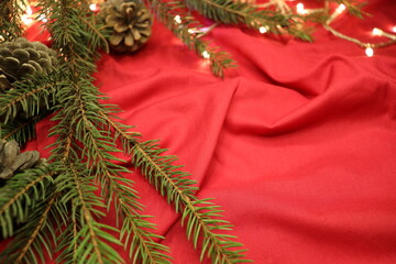 fir branch with cones and a yellow garland on a red rag background