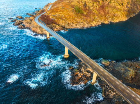 Aerial view of djupfjordbrua bridge connecting Moskenes island to the mainland, blue ocean water and rocky coastline in Lofoten archipelago, Norway at sunset. Top drone view of road, rocks in sea