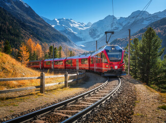 Red modern electric train traveling along a railway, winding through a stunning high mountains with...