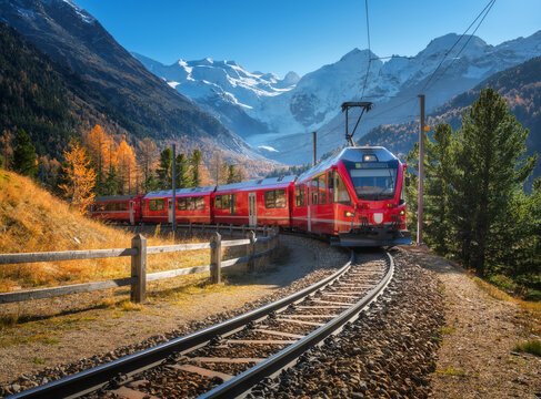 Red modern electric train traveling along a railway, winding through a stunning high mountains with snow-capped peaks and vibrant autumn trees in switzerland. Bernina Express in fall. Railway tourism