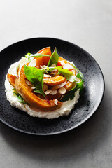 Grilled pumpkin with cream cheese, spinach, arugula and almond flakes on a black plate on concrete background. Seasonal recipe of baked Hokkaido pumpkin slices, vegetarian comfort food