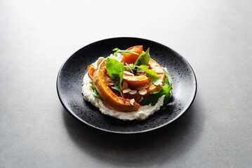 Grilled pumpkin with cream cheese, spinach, arugula and almond flakes on a black plate on concrete background. Seasonal recipe of baked Hokkaido pumpkin slices, vegetarian comfort food